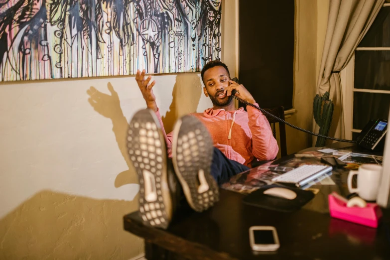 a man in an orange shirt is sitting down with his foot on the table