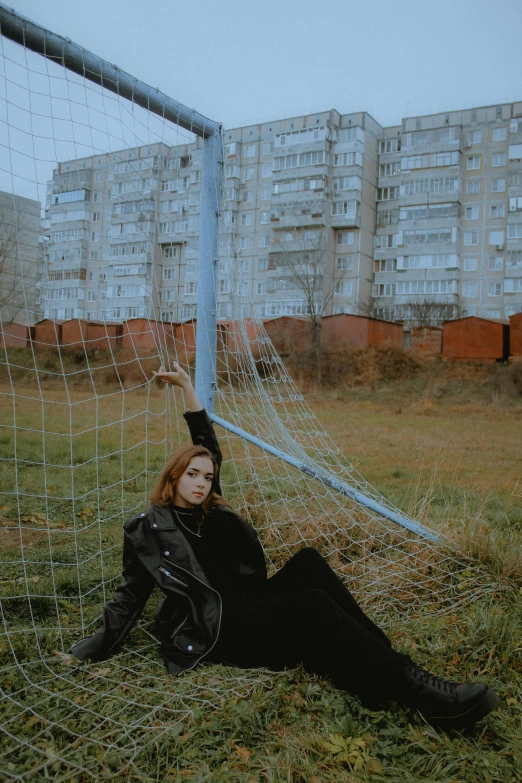 a young woman is sitting in the grass by a net