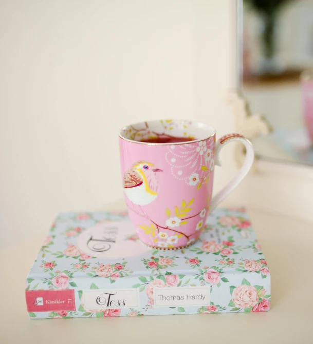 the pink flowered cup is on top of a book