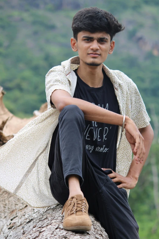 young man sitting on tree stump near mountains