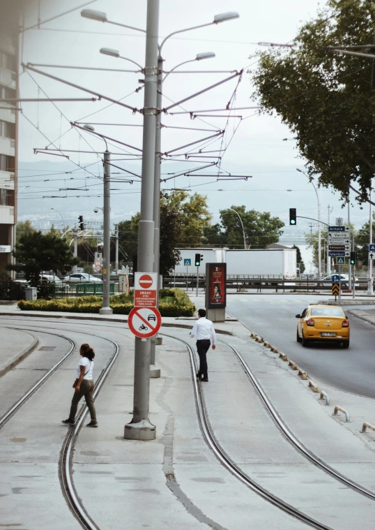 a couple of people are standing on the sidewalk near railroad tracks