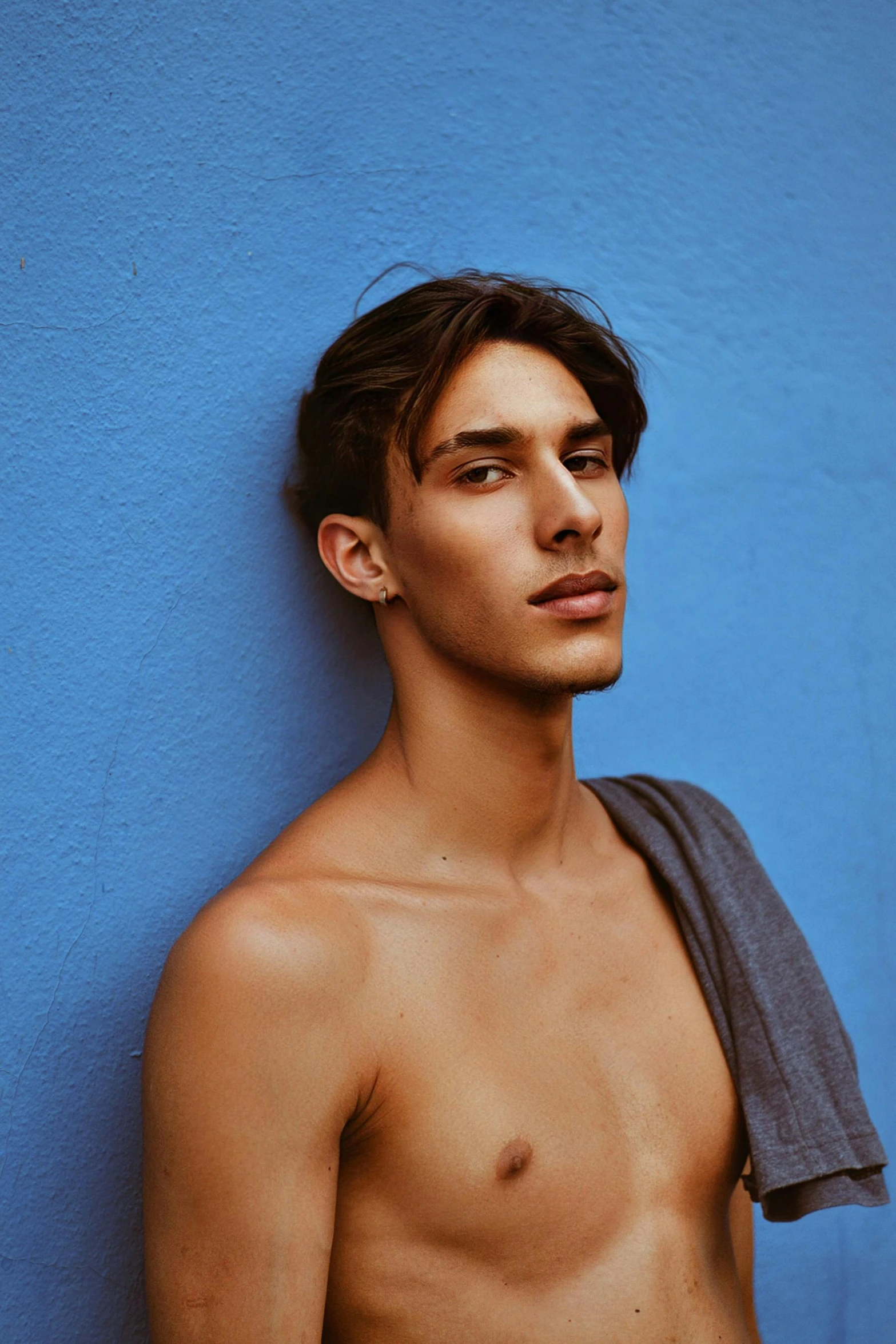 a shirtless man leans against a blue wall