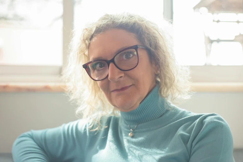 woman in green sweater and black glasses with window in the background