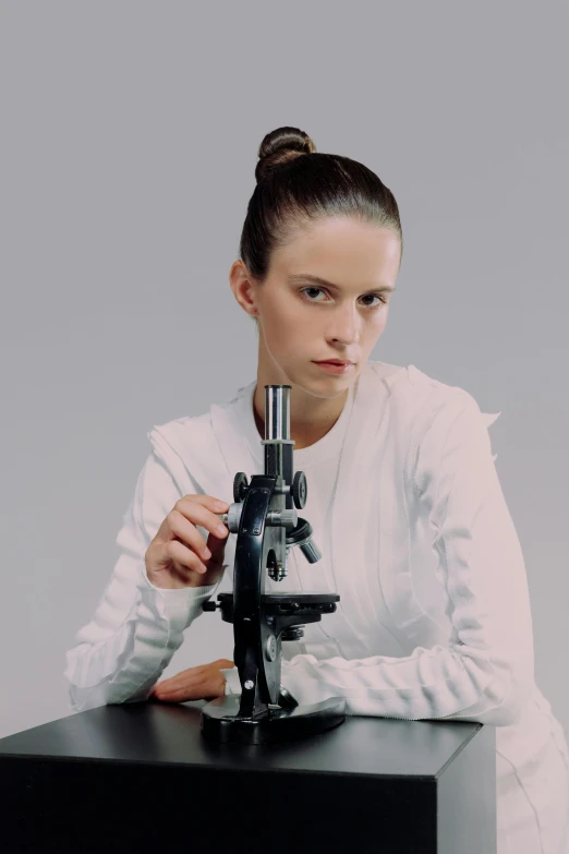 a woman with long hair sitting next to a microscope