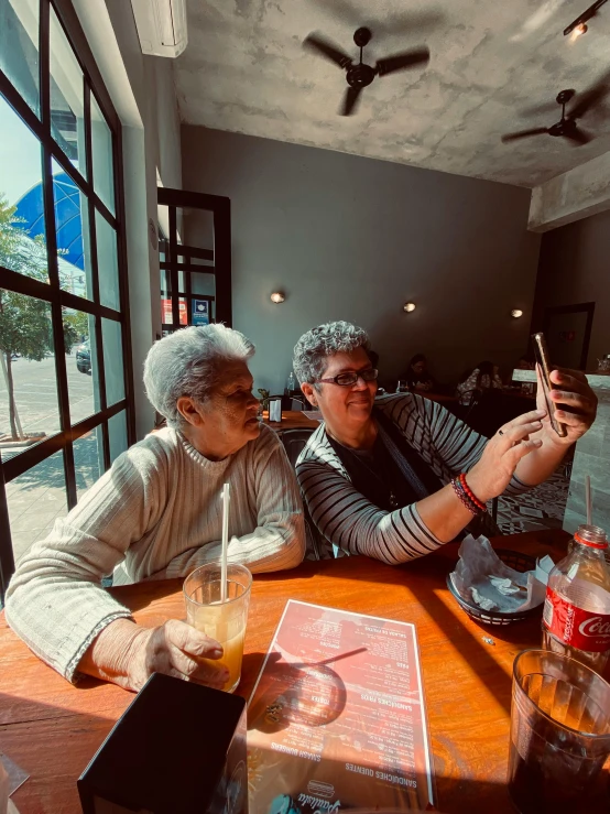 two people sitting at a table taking pictures with their phones