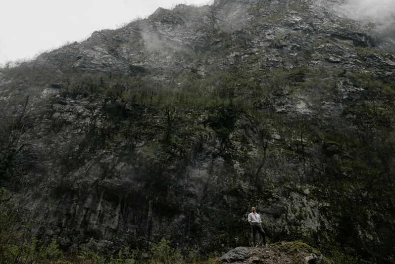 a person standing next to a tall hill in the wilderness