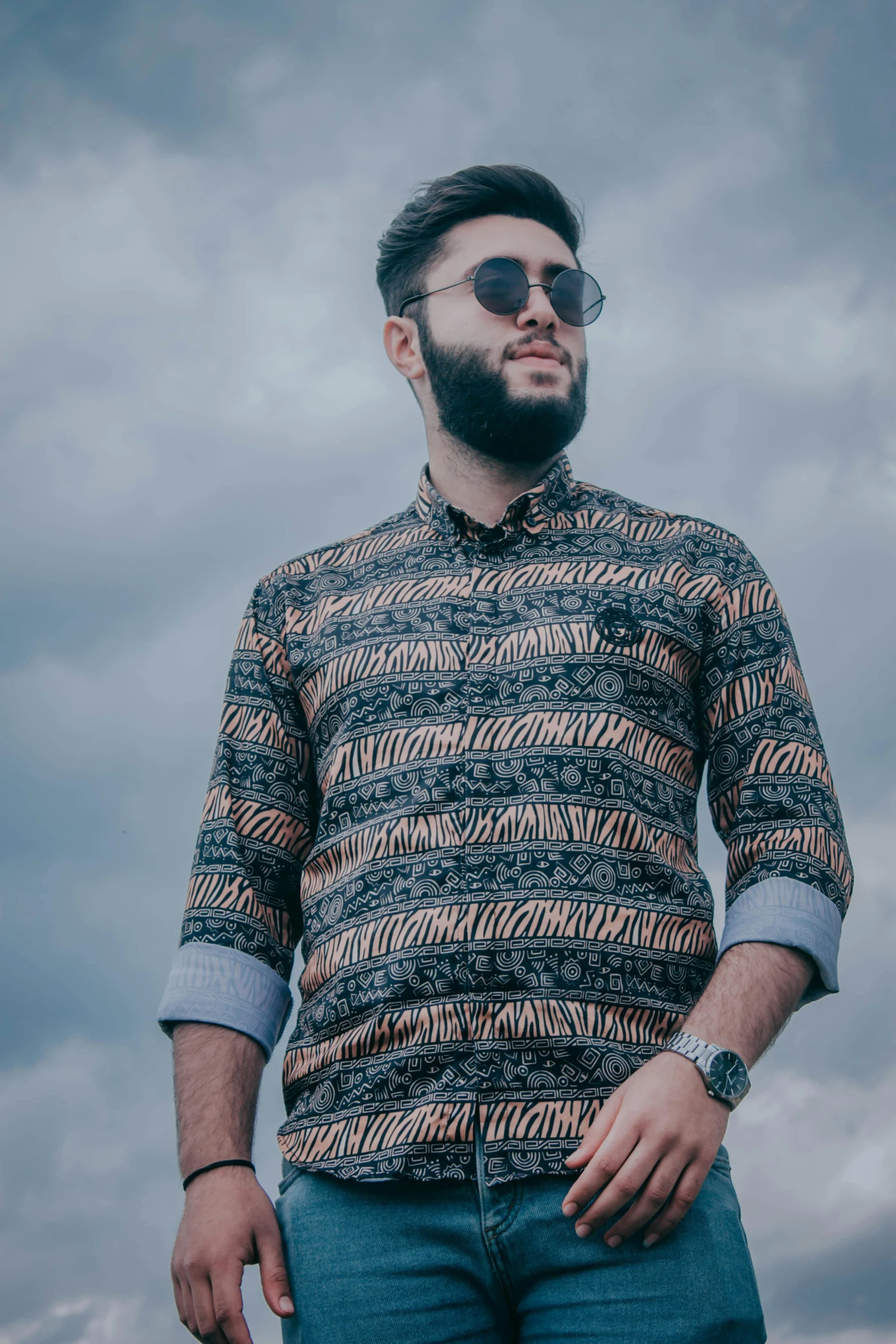 a man with a beard standing in front of a cloudy sky