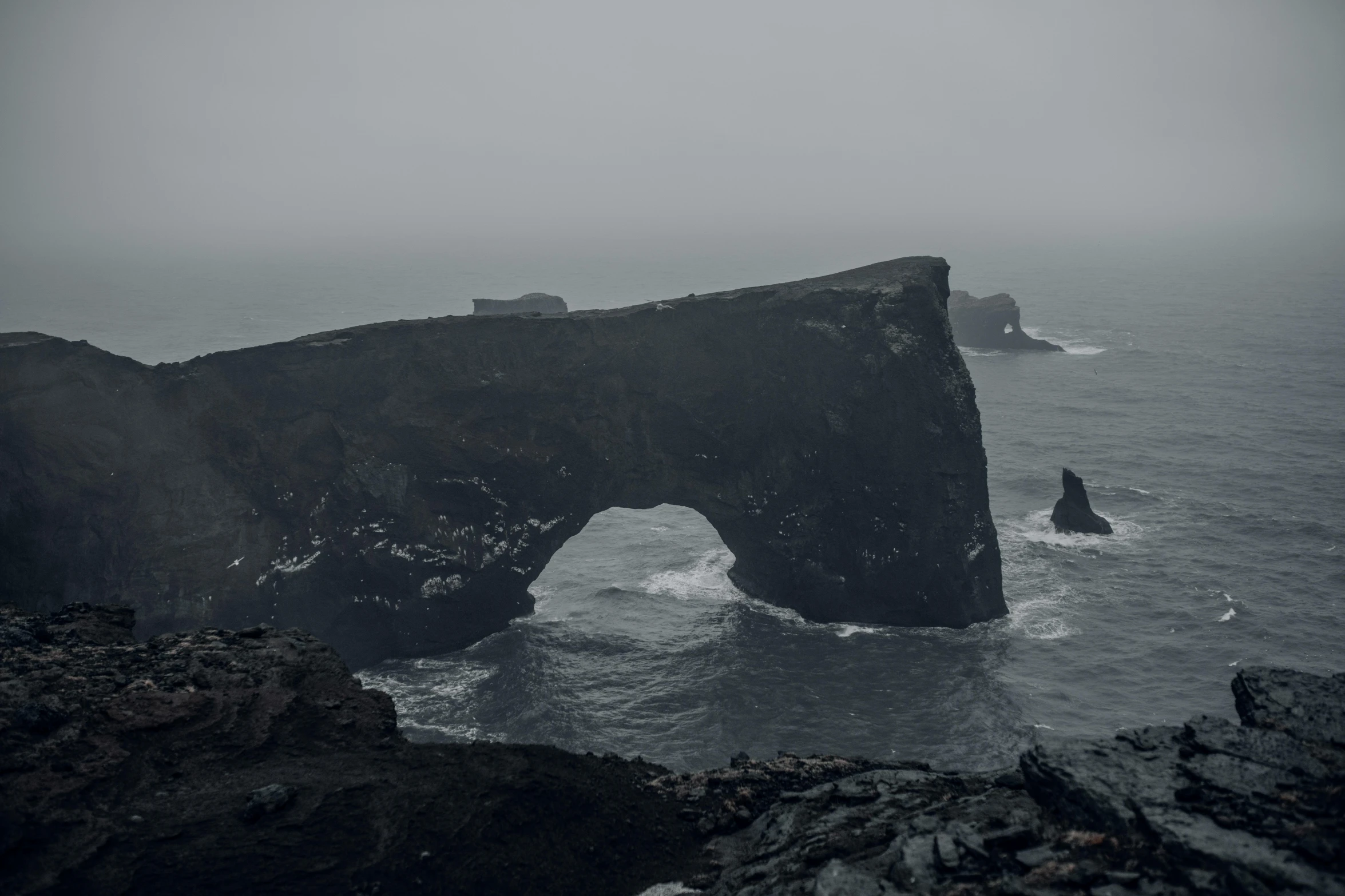 a big rock formation by the sea on a cloudy day