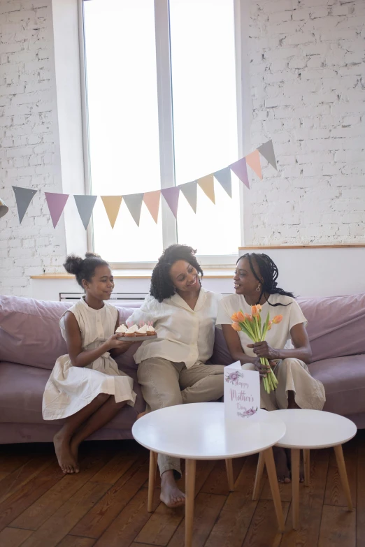 two women sit on a couch next to a little girl and cake