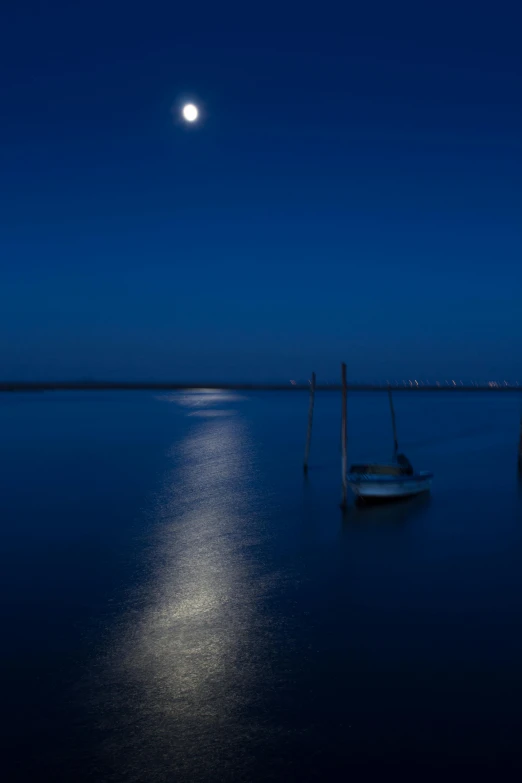 a sailboat sits in the water under a full moon