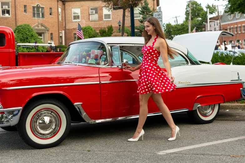 a lady in a dress next to a red classic car