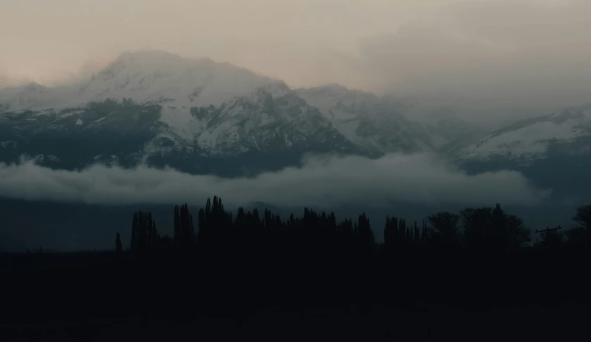 the mountains with trees under them are covered in thick, fluffy clouds