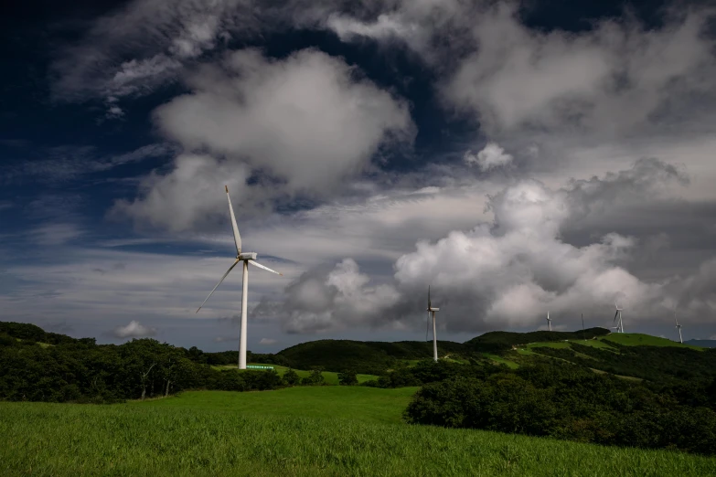 three wind mills surrounded by a forest and rolling hills