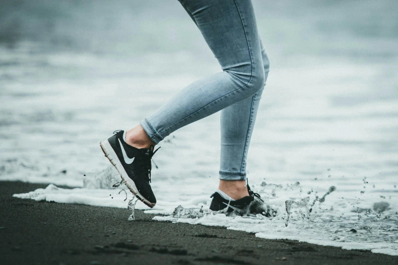 someone is walking on the shore with black sneakers