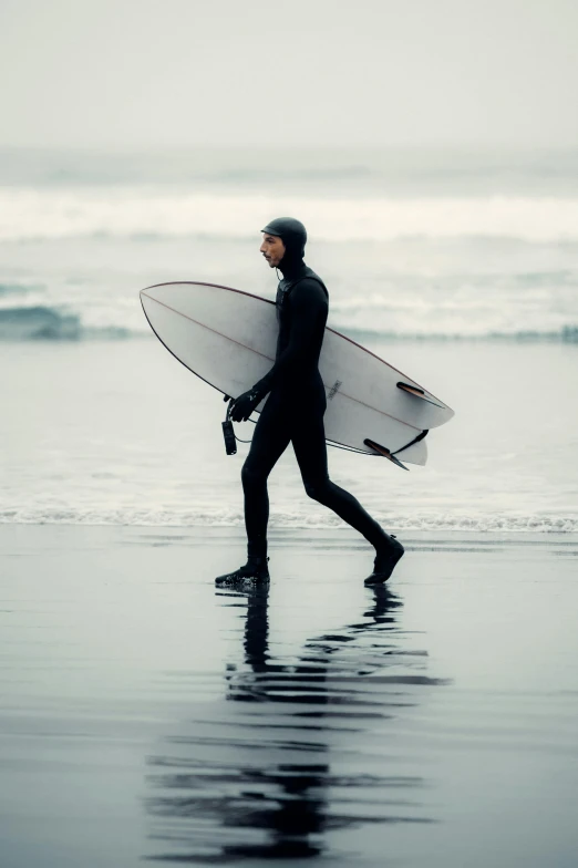 a man walking on top of a beach holding a surfboard