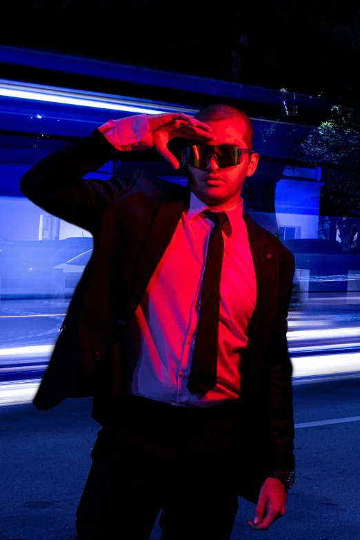 a man in a red shirt and black tie, holding sunglasses in the dark