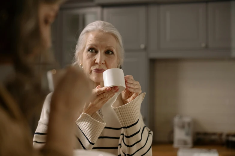 an old woman drinking coffee while looking at her reflection