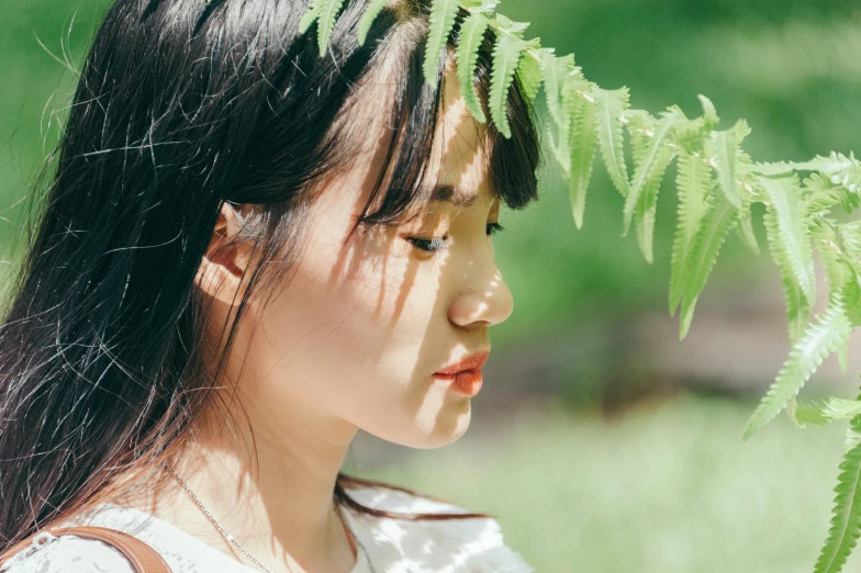 a young woman wearing a white dress looking off to the side with green foliage on her head