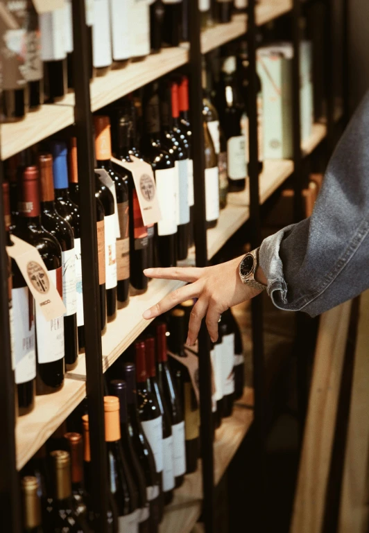 someone is holding their finger in the middle of a large rack of bottles of wine