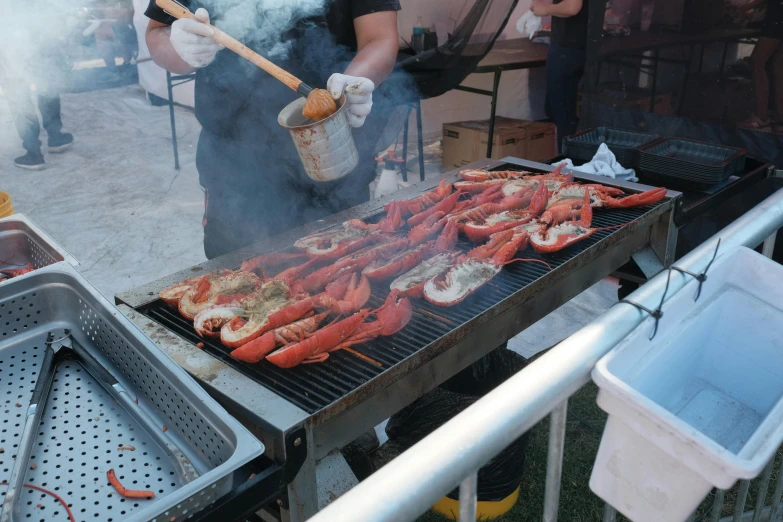 there is a man that has a large amount of lobsters on the grill