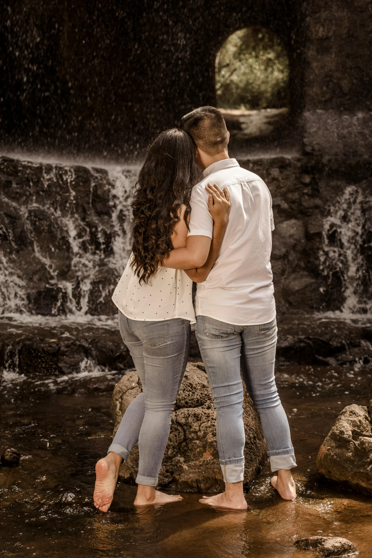 the couple hug each other next to a waterfall