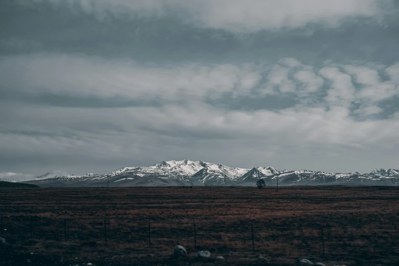 a barren grassy field with snow capped mountains in the background