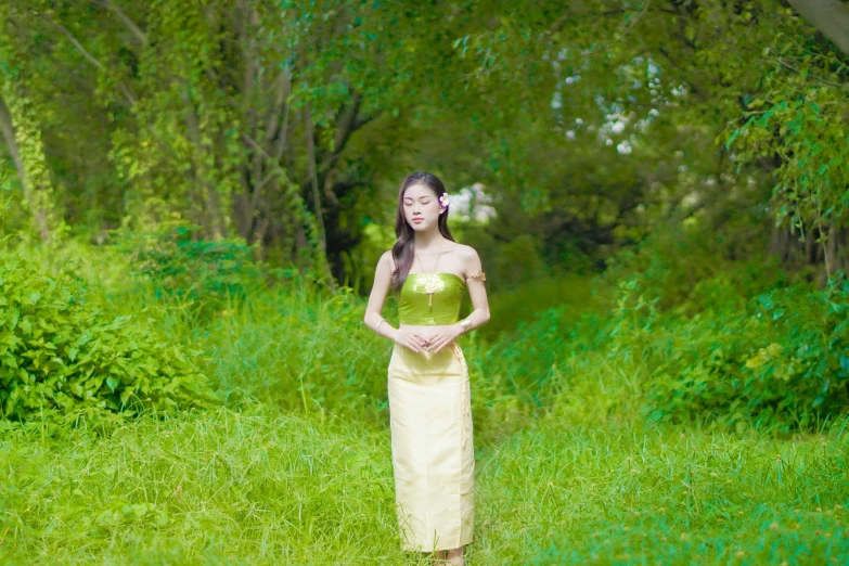 a woman stands on grass in front of trees
