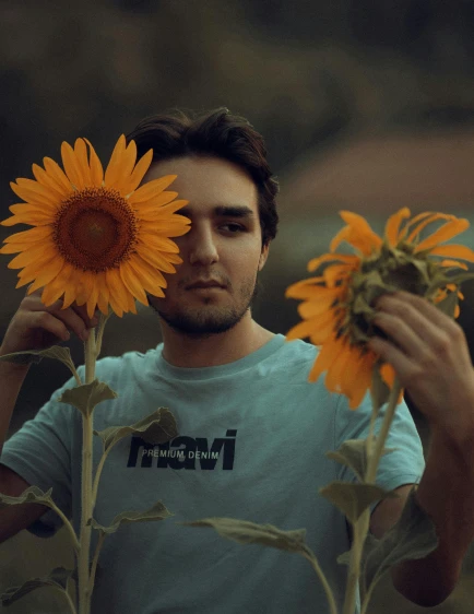 a man holding two sunflowers in front of his face