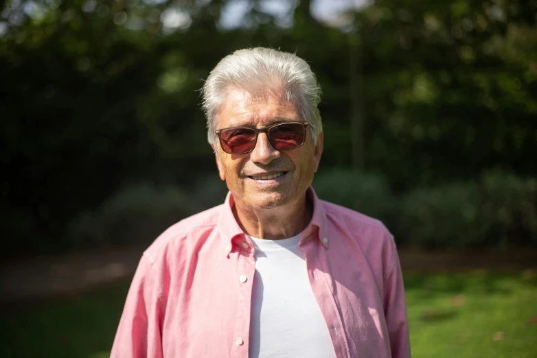 an older gentleman in pink shirt posing with trees in background