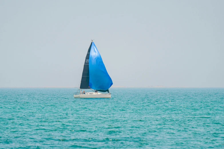 a single blue sailboat in the ocean on a sunny day