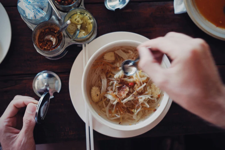 two hands holding spoons near a bowl of food