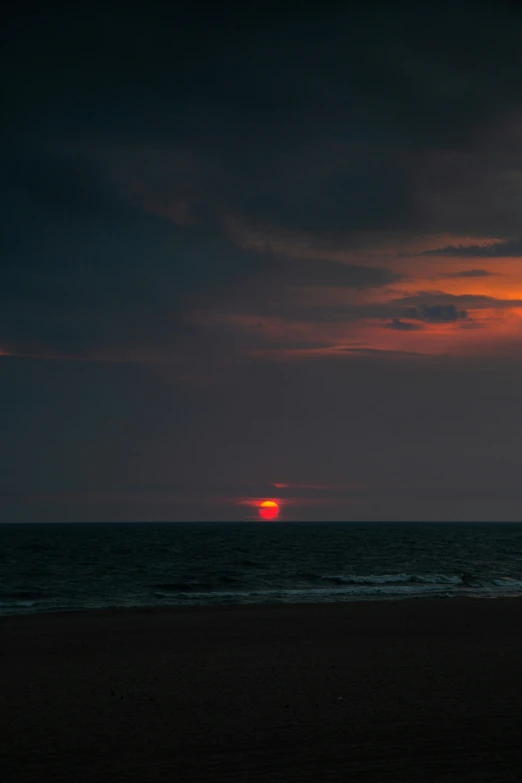 a sunset at the beach, with a lone surfer out in the water