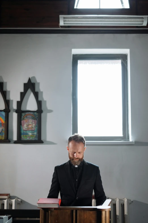 the priest is sitting behind his desk looking at paper