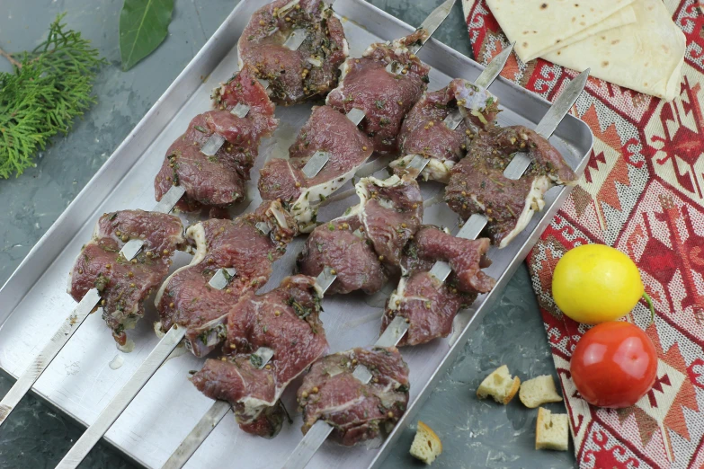 a tray of skewered meat on a stick next to a lemon, tomato and some pita chips