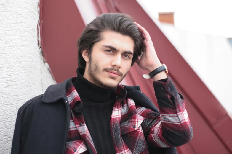 a man with black hair and a checkered vest is leaning on a wall