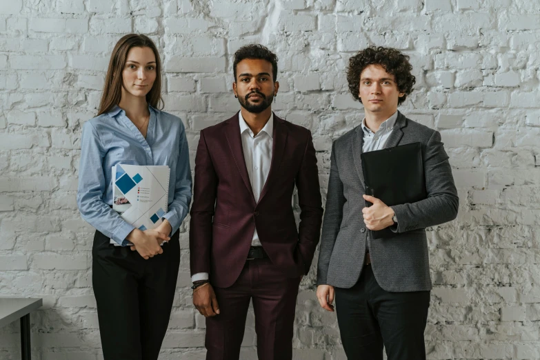 three men and one woman in suits standing next to a brick wall