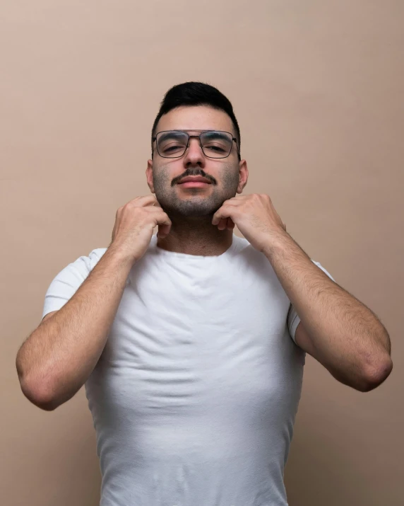 a man with glasses poses in front of a beige wall