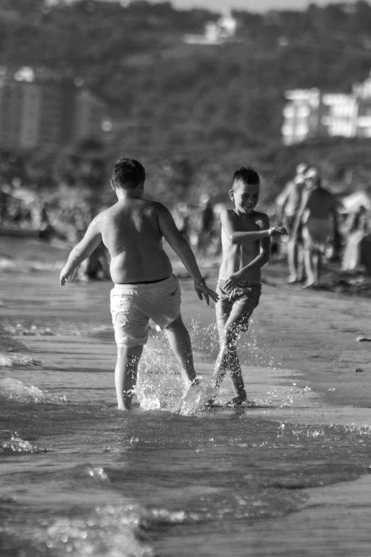 the boy walks in the water while another plays in the beach