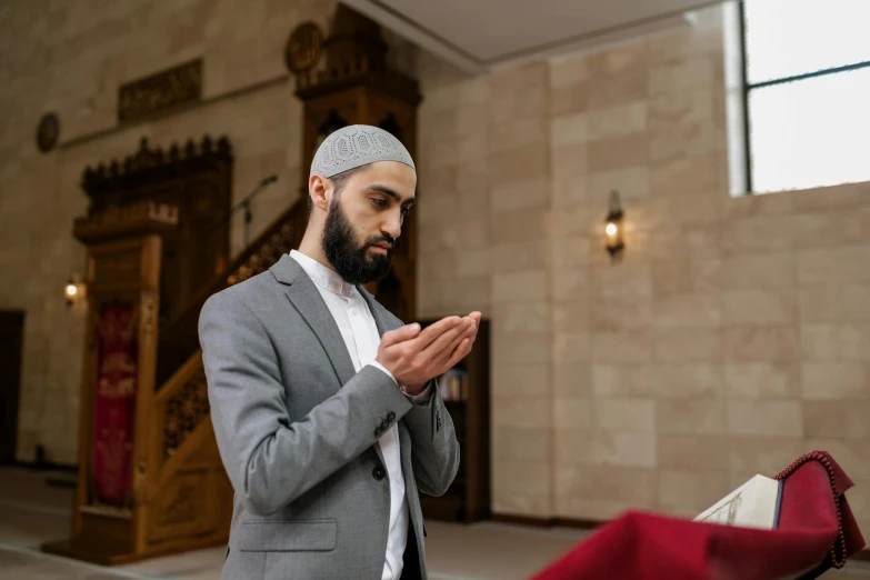 a young man dressed in a grey suit and turban is praying