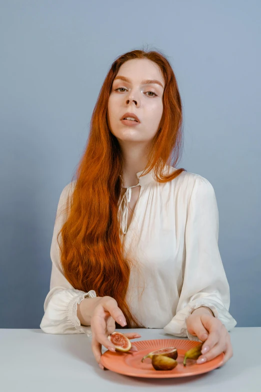 a woman with red hair sits at a table and holds an orange plate