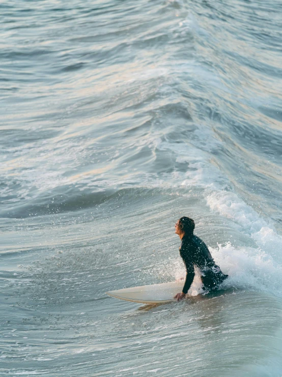 man with black wetsuit riding a white surfboard on the beach