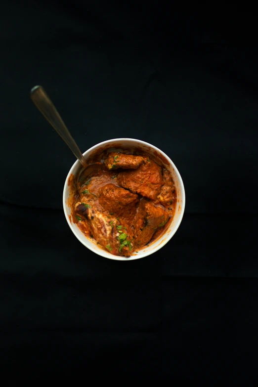 a black background with a white bowl with chicken curry and a spoon