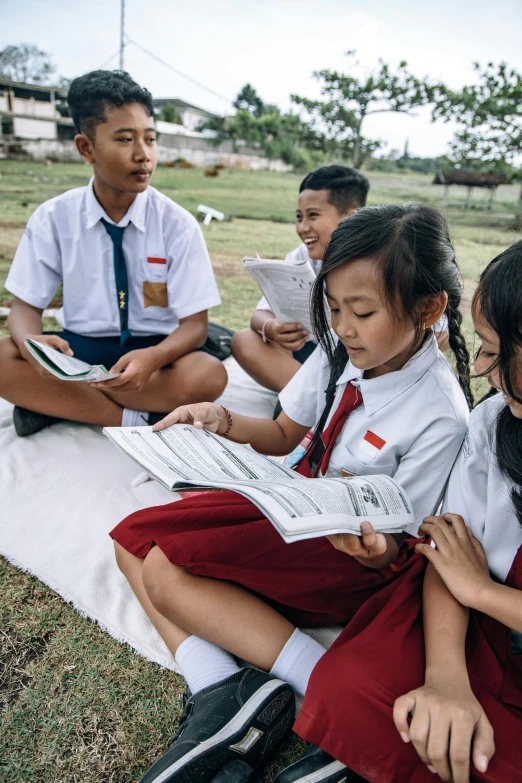 school children with book in lap on grass