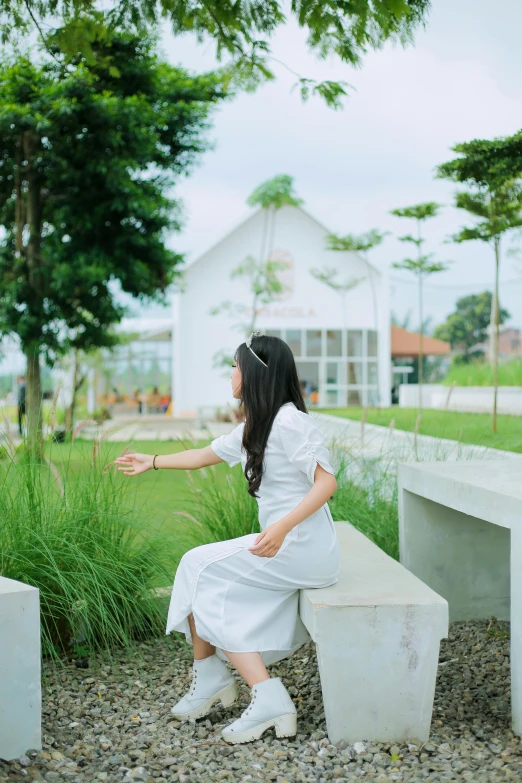 a girl is sitting on a cement bench in a white dress