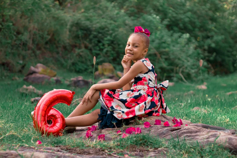 a little girl sits on the grass near a garden