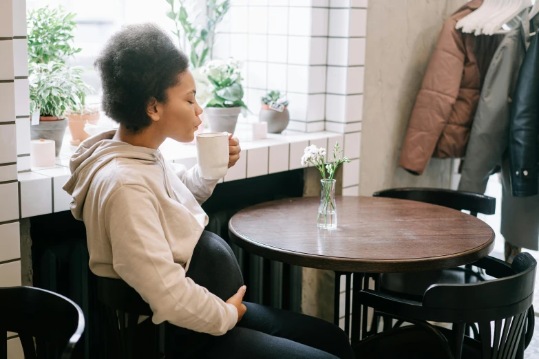 a woman sits in front of a window with a cup in her hand