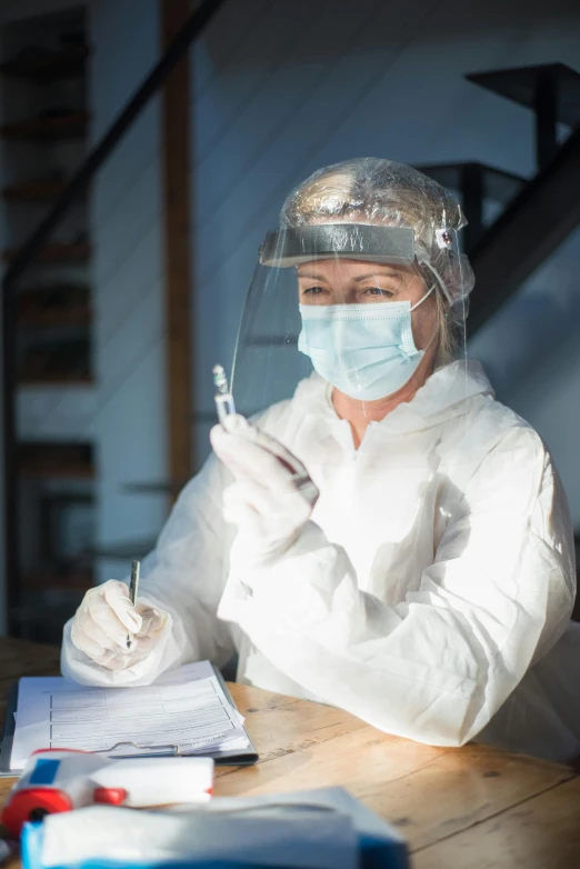 a woman in white lab coat holding a pencil and wearing face mask