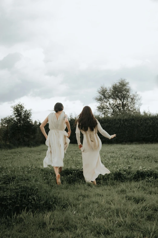 two women running through the grass on a cloudy day