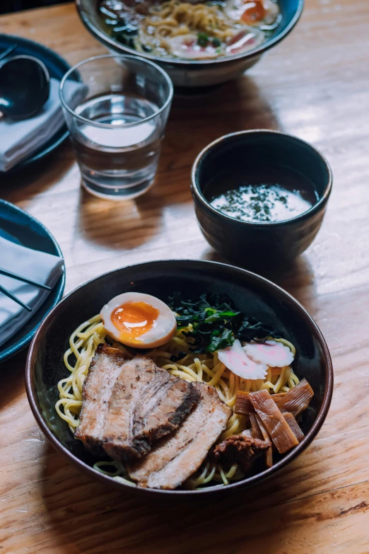 a bowl of noodles, meat and an egg on a table