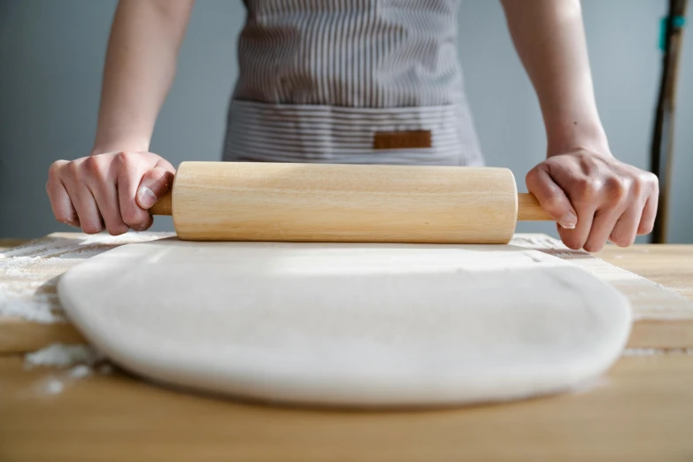 person rolling dough out on table in room